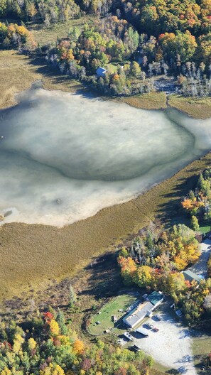 An aerial view of a lake surrounded by autumn-colored trees and a small building with a parking area.