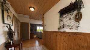 Een gang met houten vloer, een houten bankje, een deur en een muur met een decoratief vistnet.
