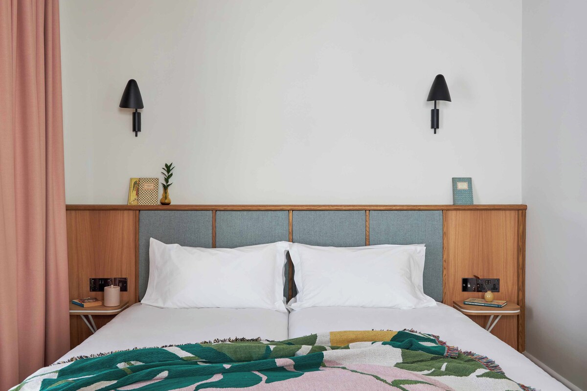 A neatly made bed with a patterned blanket, two bedside tables with lamps, and a headboard with a shelf.