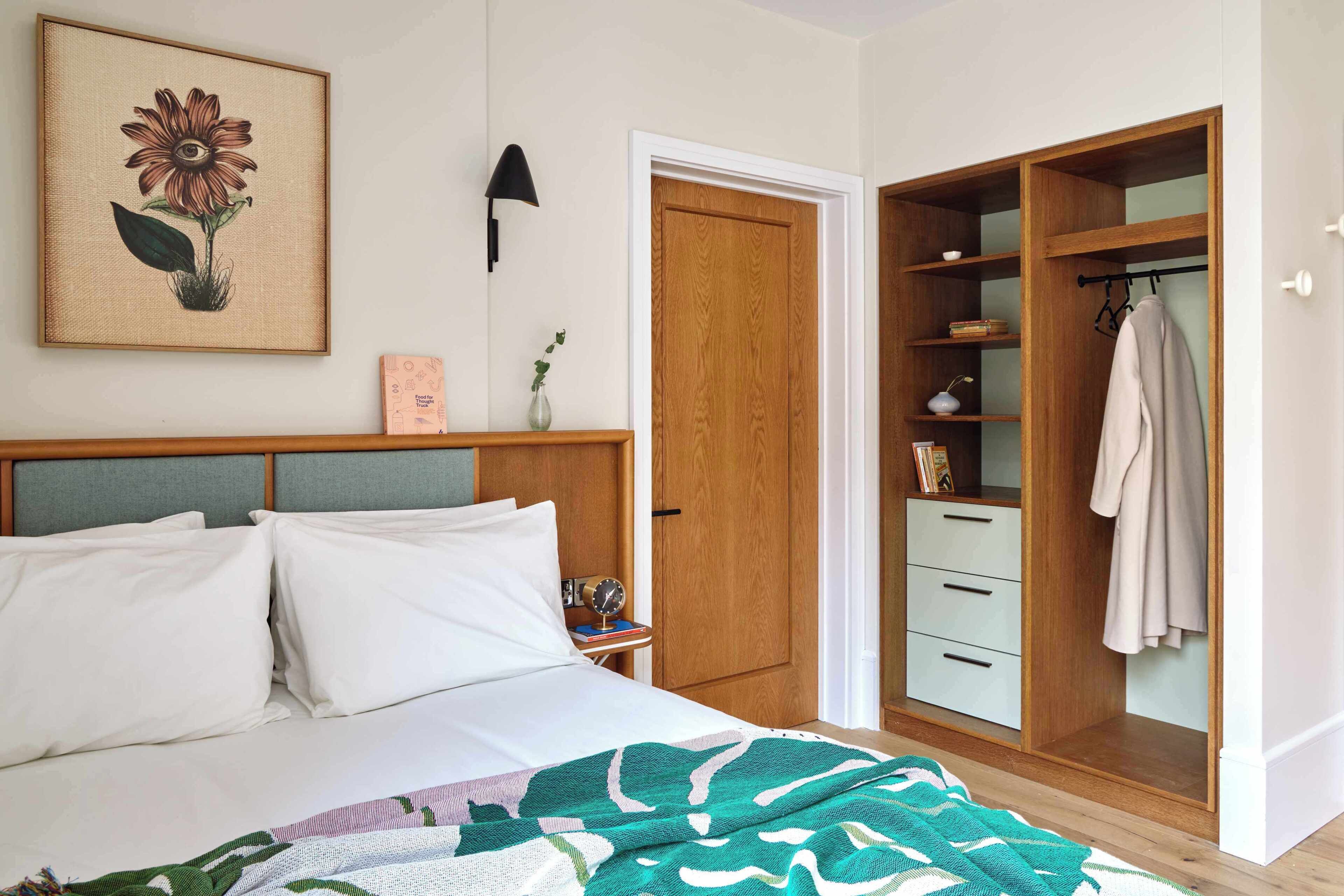 Un dormitorio con cama, mesita de noche, cuadro enmarco, armario y puerta.