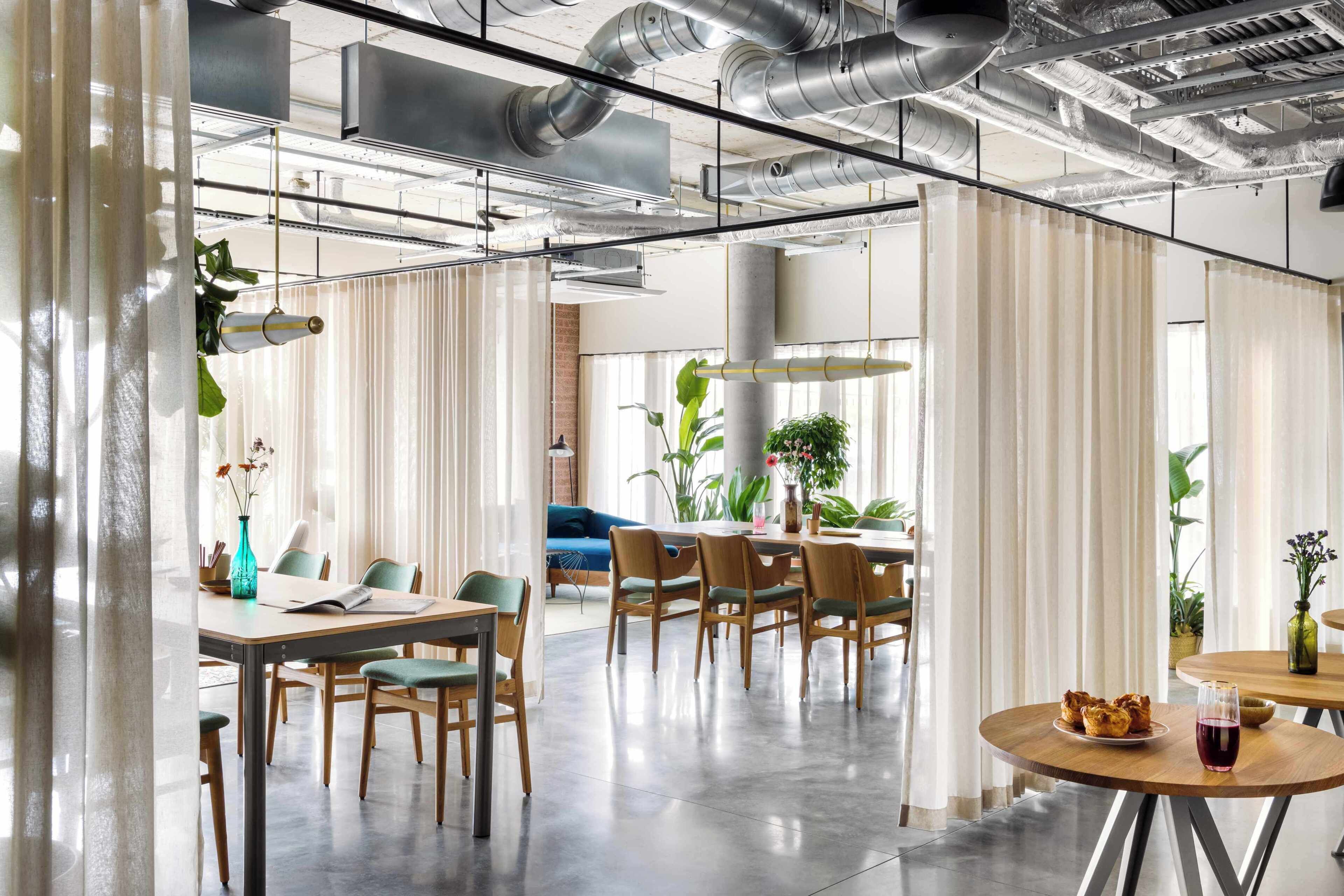 A modern office space with a dining area, meeting tables, and a large window with curtains.
