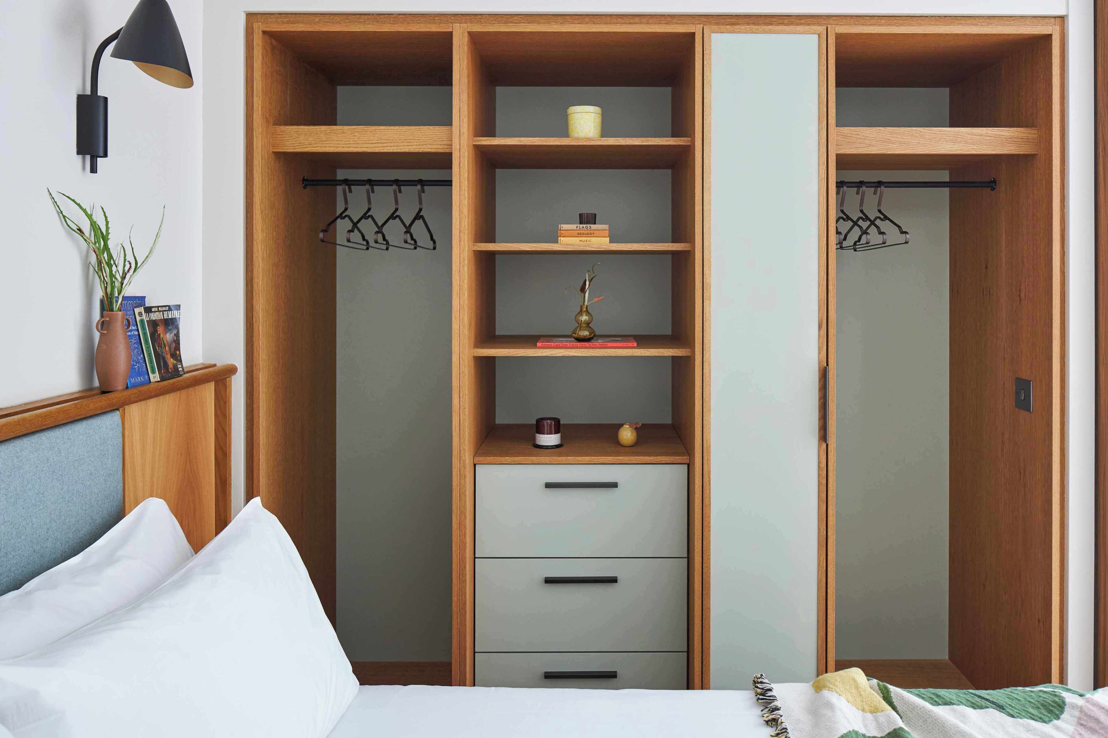 A bedroom with a bed, a nightstand, a wardrobe with multiple compartments, and a wall-mounted lamp.