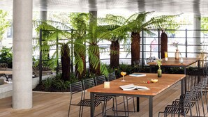 A spacious indoor dining area with a long wooden table, black metal chairs, and lush green plants. - Turing Locke Cambridge (Cambridge)