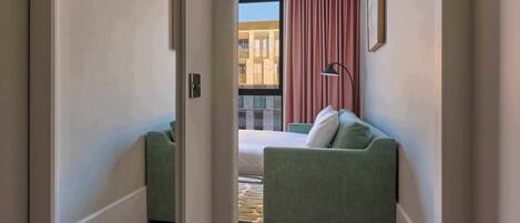 Een hotelkamer met een bed, een groene bank, een raam met gordijnen en uitzicht op een gebouw.