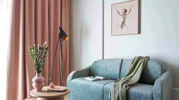 A living room with a sofa, a lamp, a vase with plants, and a framed picture on the wall.