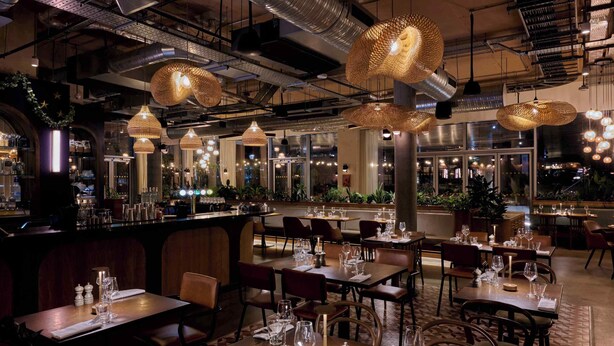 A restaurant with multiple dining tables, hanging wicker lamps, and a bar area. - Turing Locke Cambridge (Cambridge)