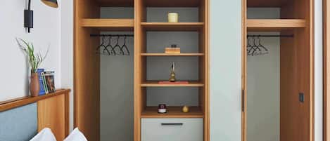 A bedroom with a bed, a nightstand, a wooden wardrobe with multiple shelves and drawers, and a wall-mounted lamp.