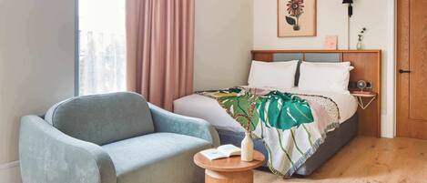 Un dormitorio con cama, sofá, mesita de noche y ventana con cortinas.