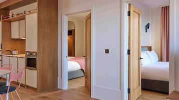 A hotel room with a kitchenette, a bed with a pink blanket, and a bathroom with a shower curtain.