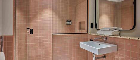 Un baño con ducha, lavabo, espejo y toallero.