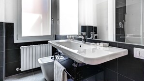 A modern bathroom with a large white sink, a mirror, and a shower area.