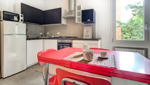 A compact kitchen with a red table, white cabinets, and a view of greenery outside.
