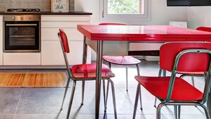 A modern kitchen with a built-in oven, a stainless steel range hood, and a red dining table with matching chairs.