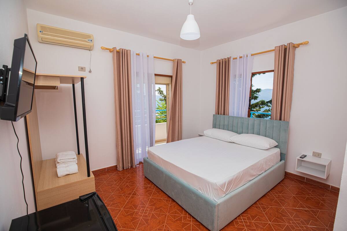 A bedroom with a bed, a TV on a stand, a heater, and a window with curtains.