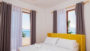 A hotel room with a bed, white linens, and a view of the sea.