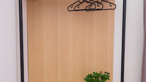 A wooden wardrobe with a hanging rod, a plant, and two glasses on top.