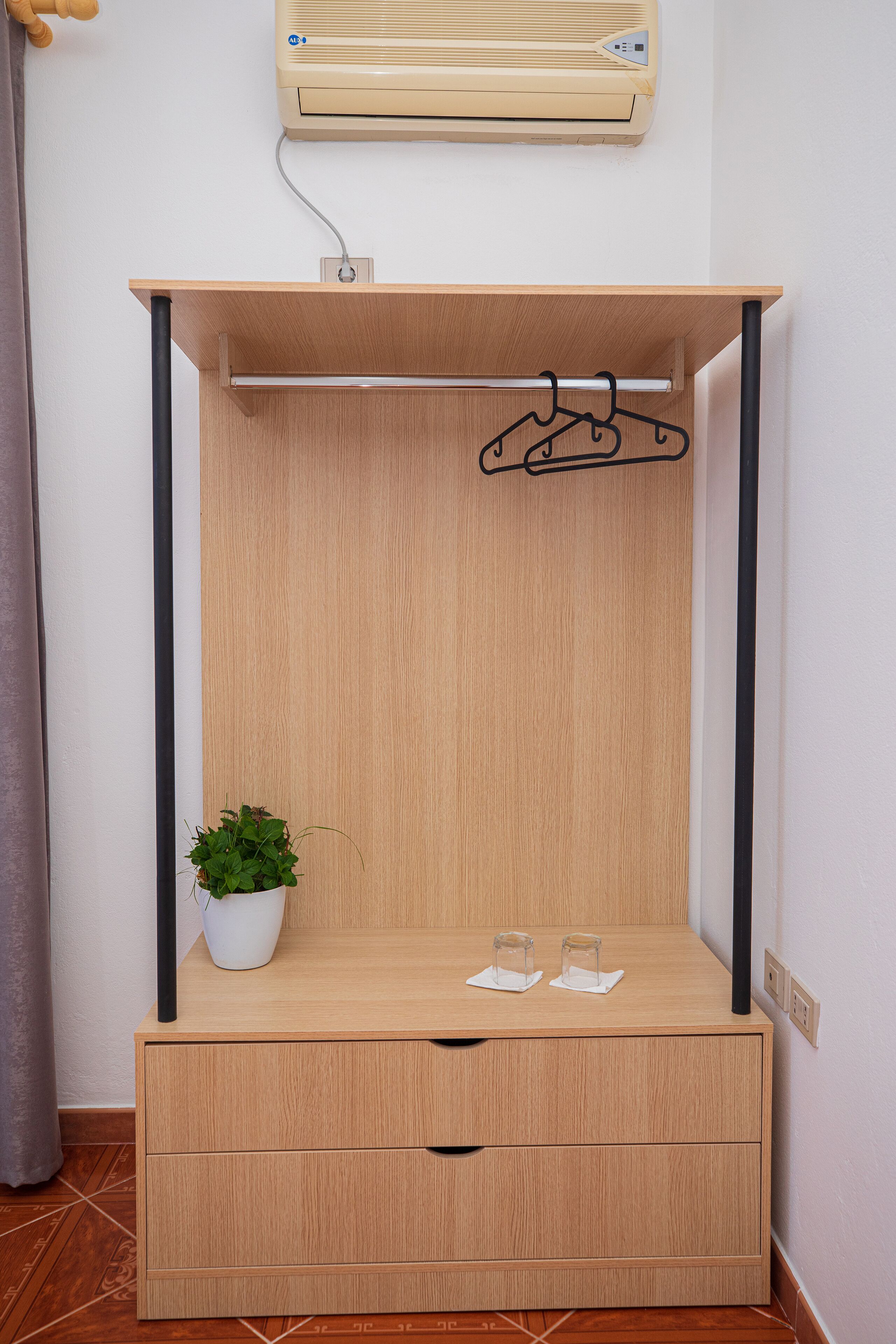 Een compacte kamer met een houten bedframe, een kleine plant in pot en een wandairconditioner.