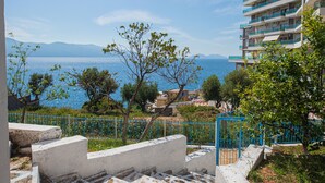 A coastal hotel with a view of the sea, a patterned terrace, and a blue fence.