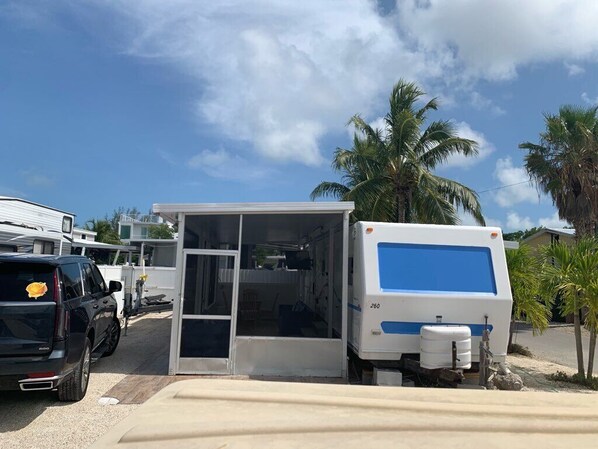 A mobile home with a sliding door, a blue and white RV parked beside it, and palm trees in the background. - RV Camper in the heart of Key Largo (Key Largo)