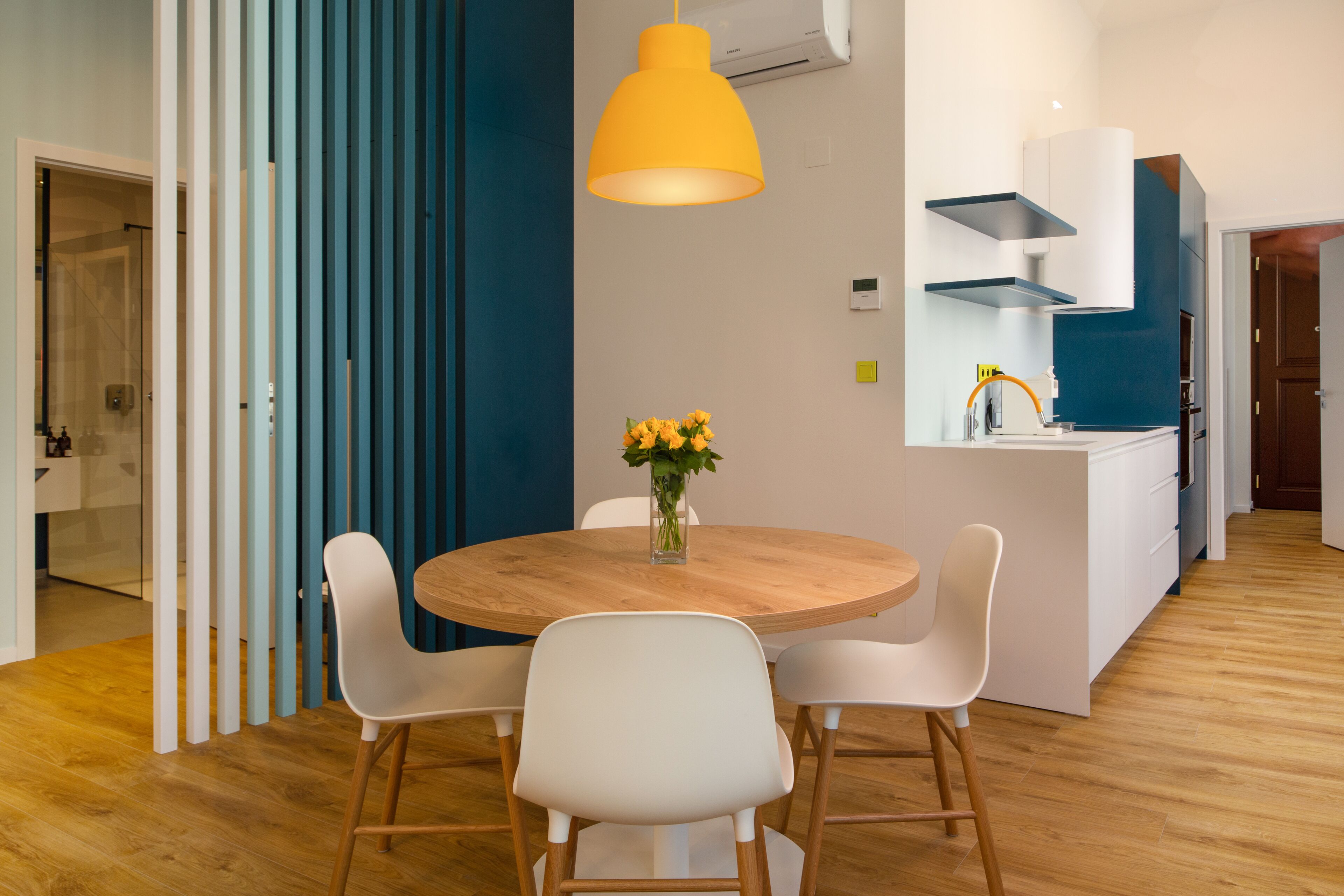 Una cocina moderna con armarios blancos, una mesa de comedor de madera y una lámpara colgante amarilla.