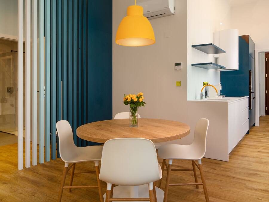 Una cocina moderna con armarios blancos, una mesa de comedor de madera y una lámpara colgante amarilla.