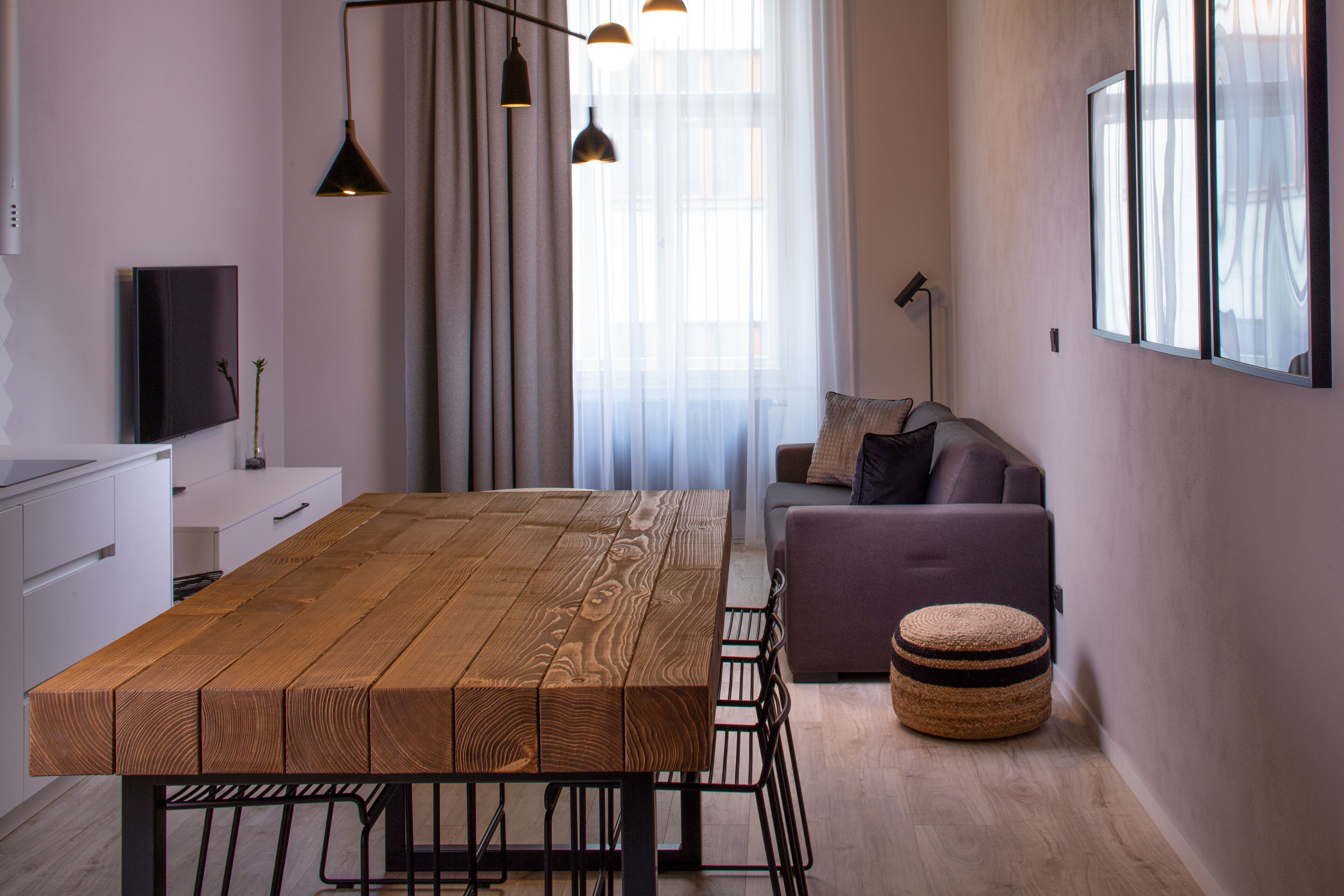 Un espacio de estar moderno con una mesa de comedor de madera, un sofá y un otoman pequeño y redondo.