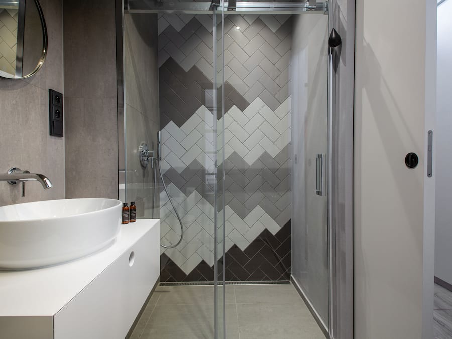 A modern bathroom with a large white sink, a glass-enclosed shower, and a herringbone-patterned tile wall.