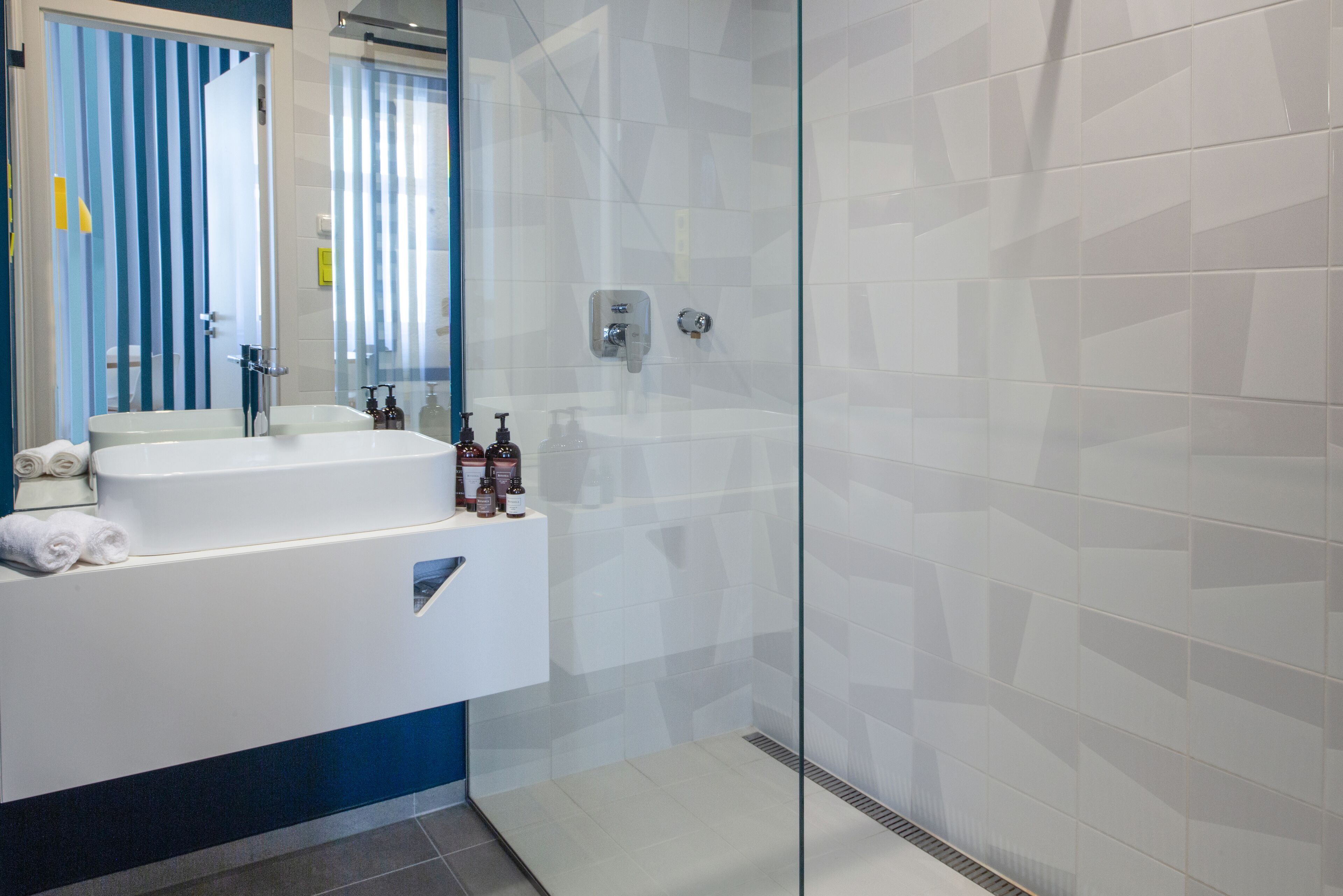 A modern bathroom with a glass shower enclosure, a white sink with a mirror, and toiletries on the counter.