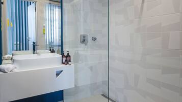 A modern bathroom with a glass shower enclosure, a white sink with a mirror, and toiletries on the counter.