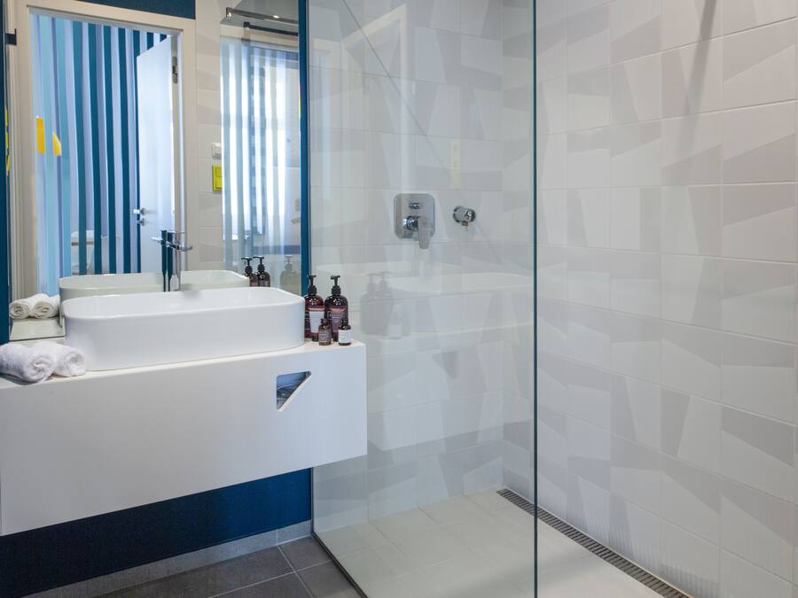 A modern bathroom with a glass shower enclosure, a white sink with a mirror, and toiletries on the counter.