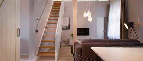 A modern interior with a staircase, a sofa, a dining table, and pendant lighting.