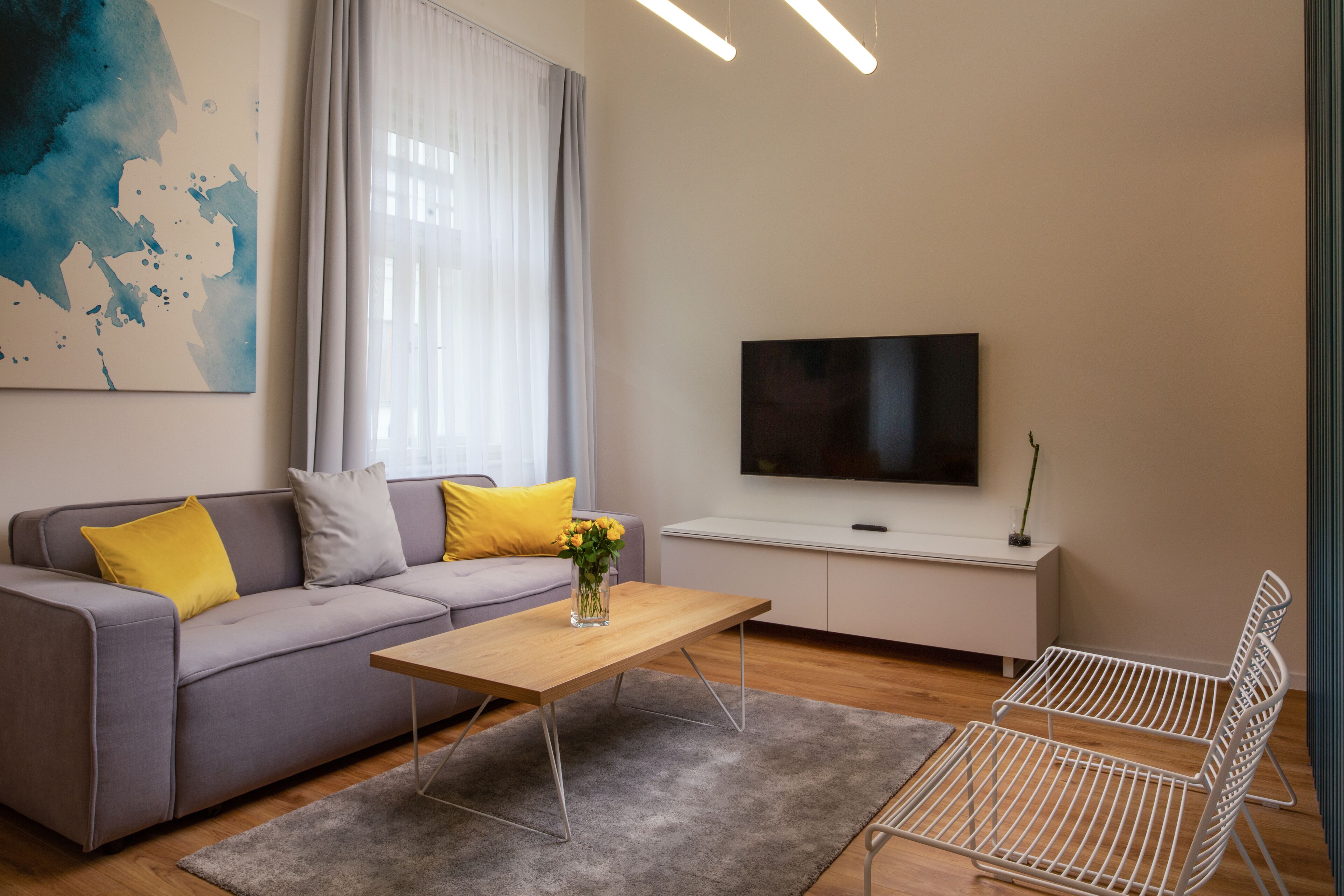 Una sala de estar moderna con sofá, mesa de centro, televisor y sillas de metal.