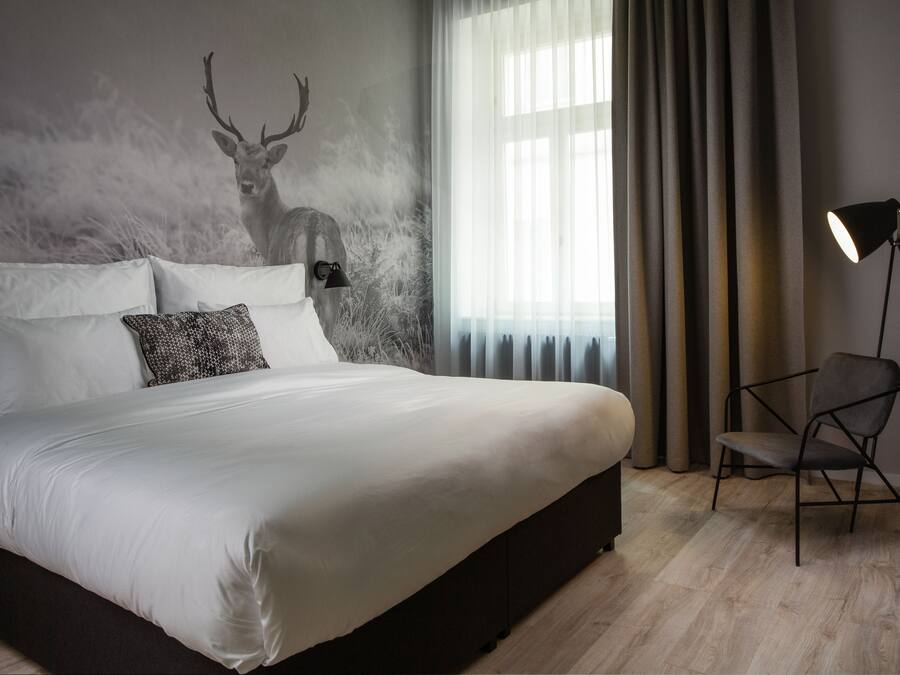 A modern bedroom with a large bed, a chair, a lamp, and a wall mural of a deer.
