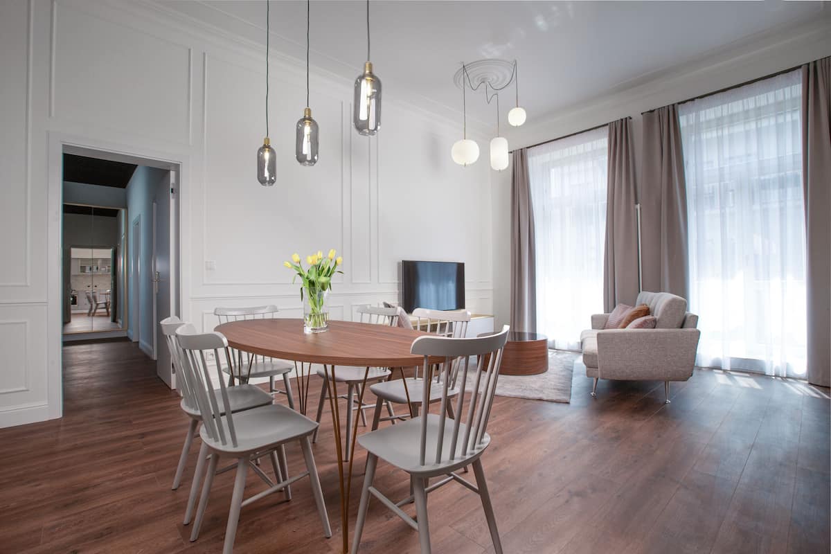 A modern living room with a dining area, featuring a wooden dining table, white chairs, a sofa, and a TV.