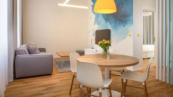 A modern living room with a round wooden table, white chairs, a grey sofa, and a yellow pendant light.