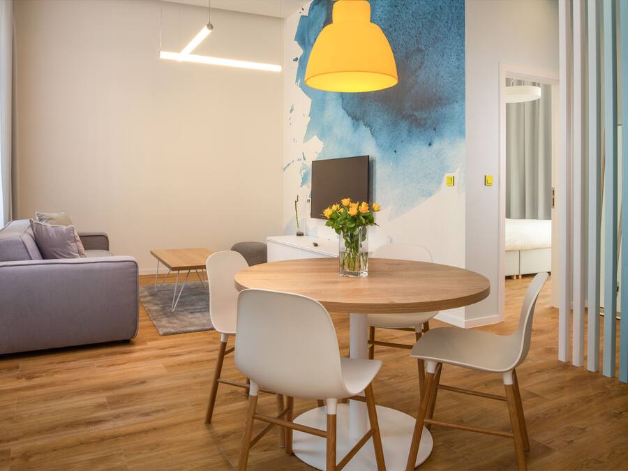 A modern living room with a round wooden table, white chairs, a grey sofa, and a yellow pendant light.