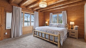 Een slaapkamer in een houten chalet met een bed, twee nachtkastjes, een raam en een plafondlamp.