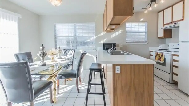 Une cuisine moderne dotée d’un îlot central, d’un coin repas avec des chaises et d’une grande fenêtre avec des stores.