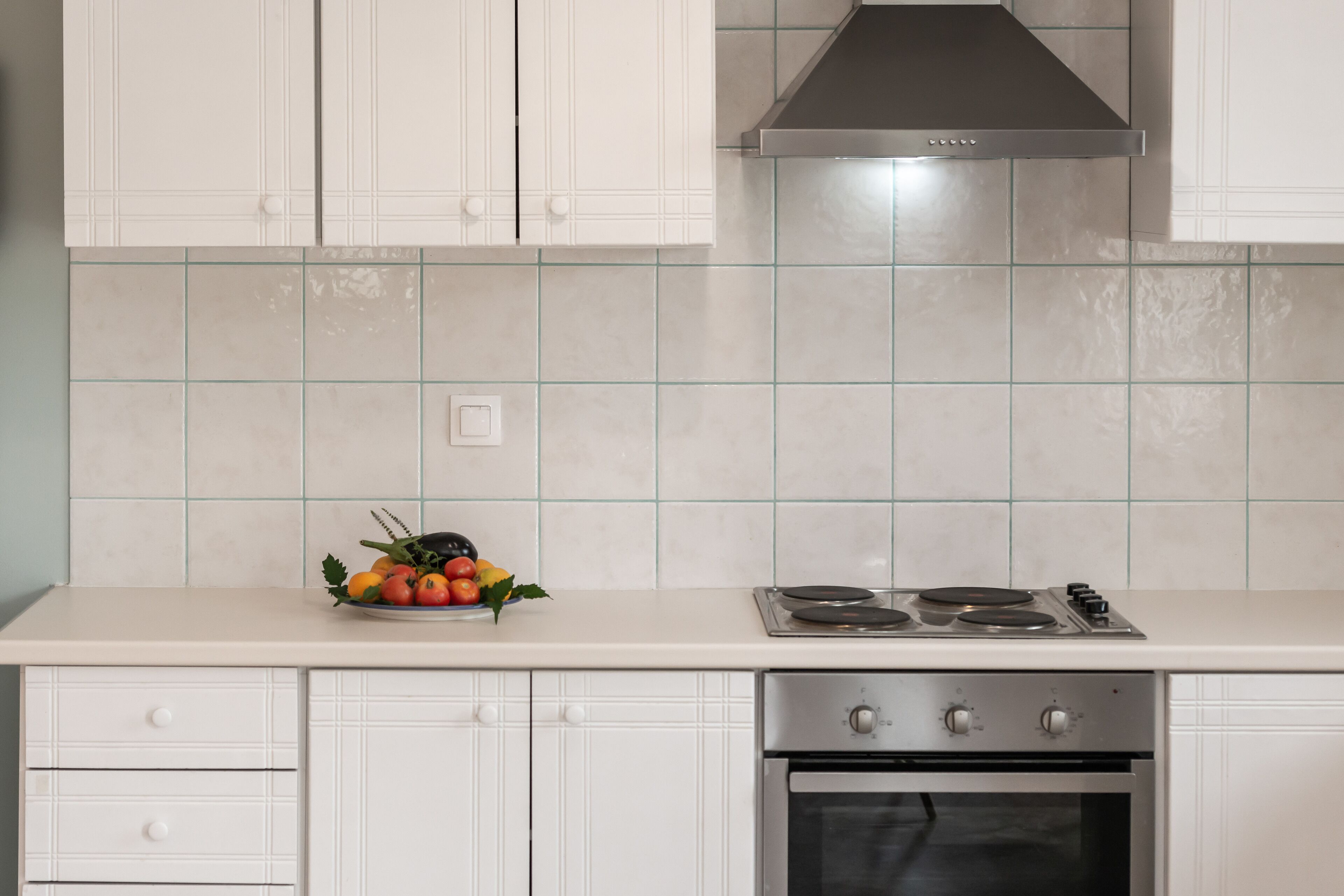 Une cuisine avec des meubles blancs, une cuisinière à gaz et un dosseret carrelé.