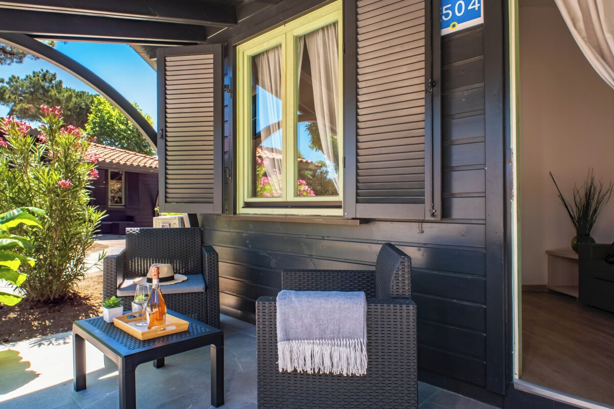 A covered outdoor seating area with wicker furniture, a table with a drink and a hat, and a window with shutters.