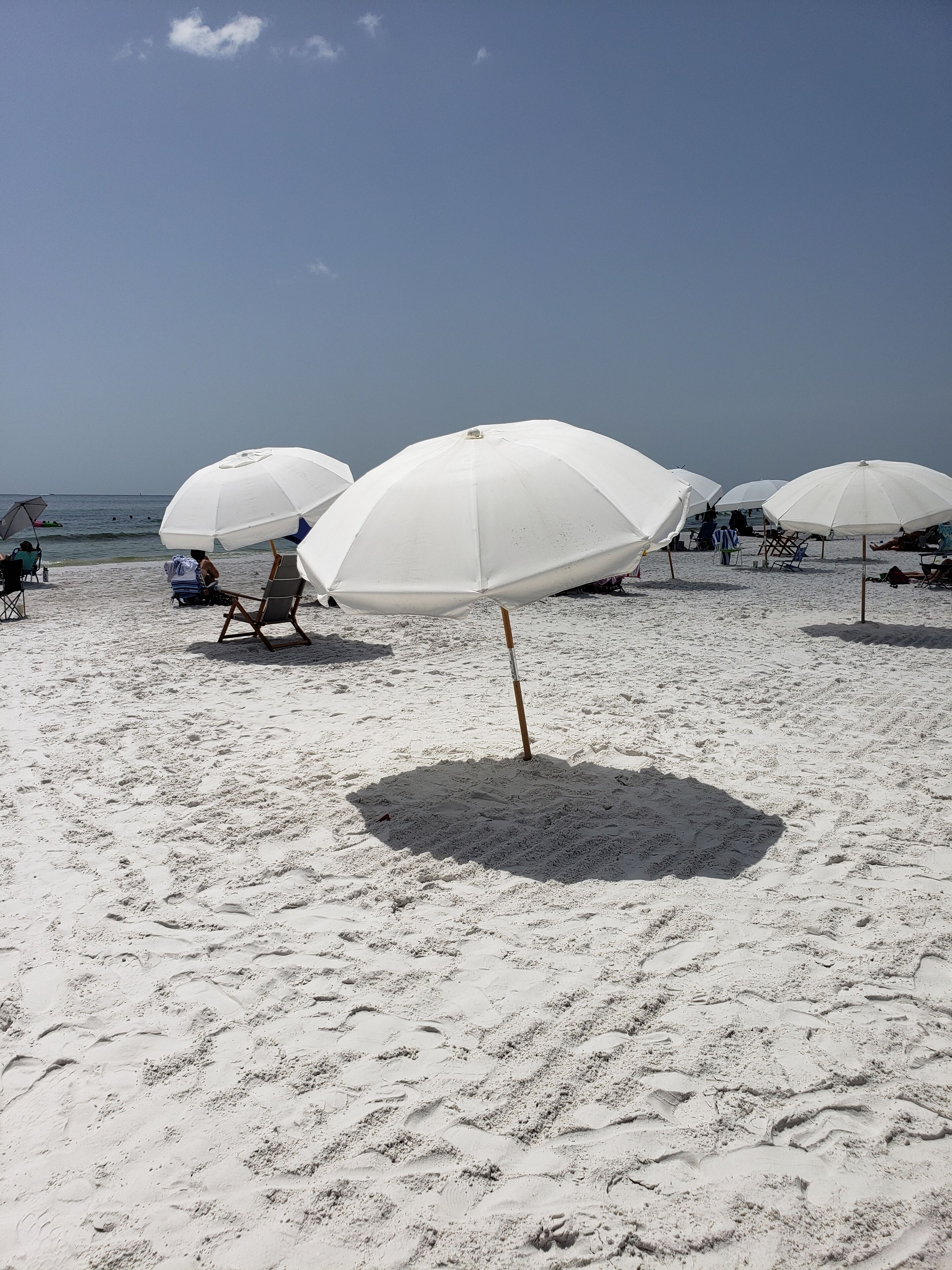 Una playa con sombrillas y sillas de playa blancas.