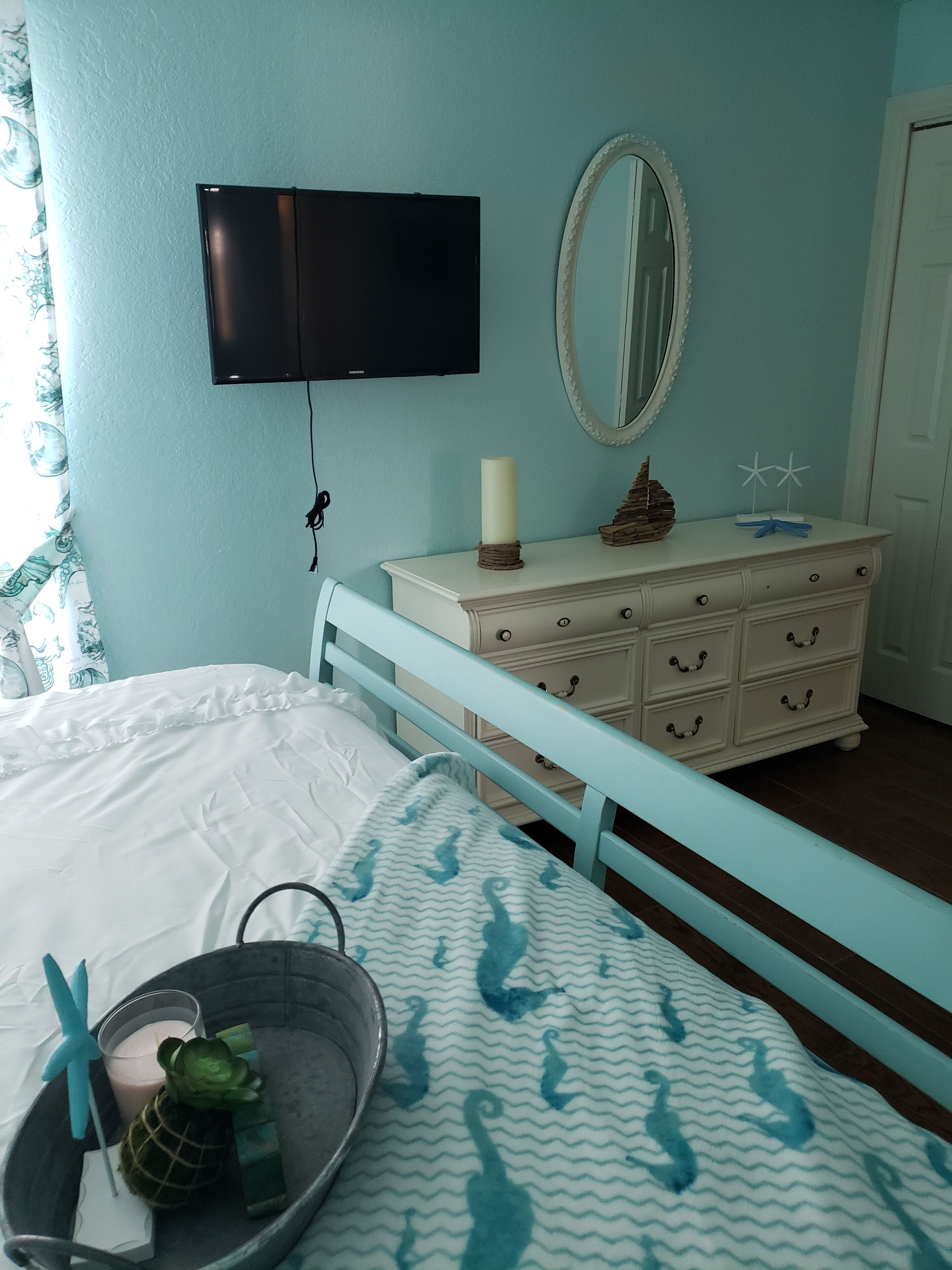 A bedroom with a bed, a dresser, a mirror, and a television on the wall.