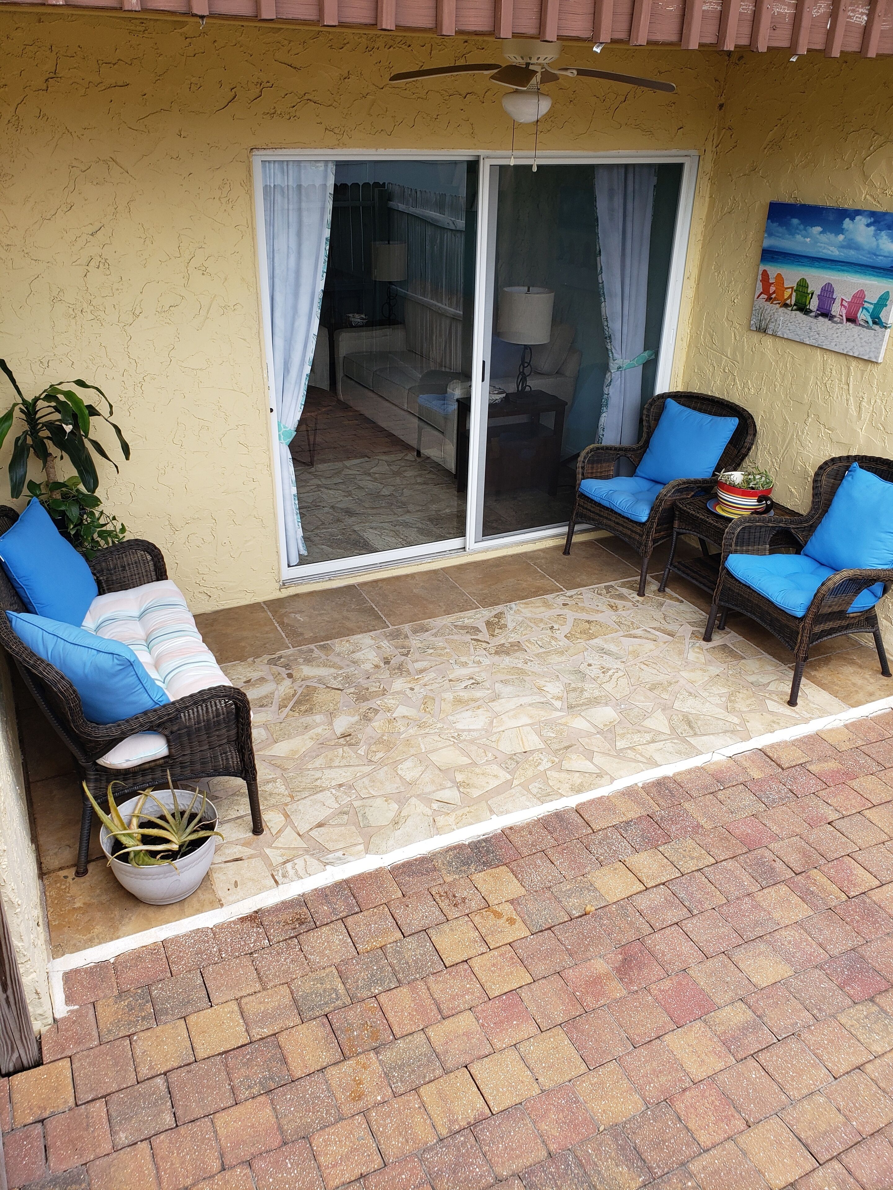 A covered patio area with wicker furniture, a ceiling fan, and a view into a room with a sofa and curtains.