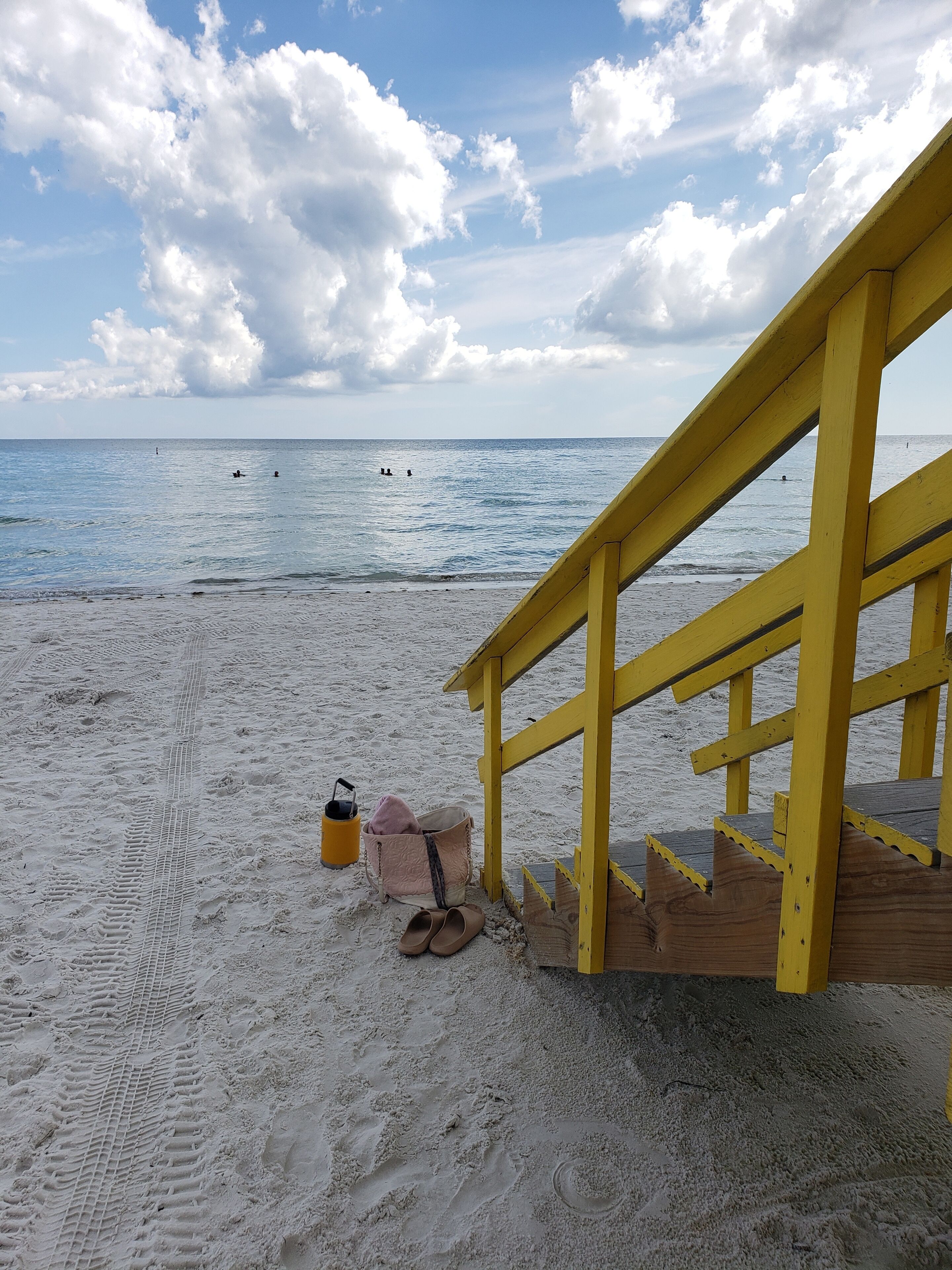 A beach with a yellow wooden structure, a sandy path, and a clear view of the ocean.