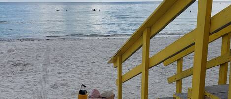 A beach with a yellow wooden structure, a sandy path, and a clear view of the ocean.