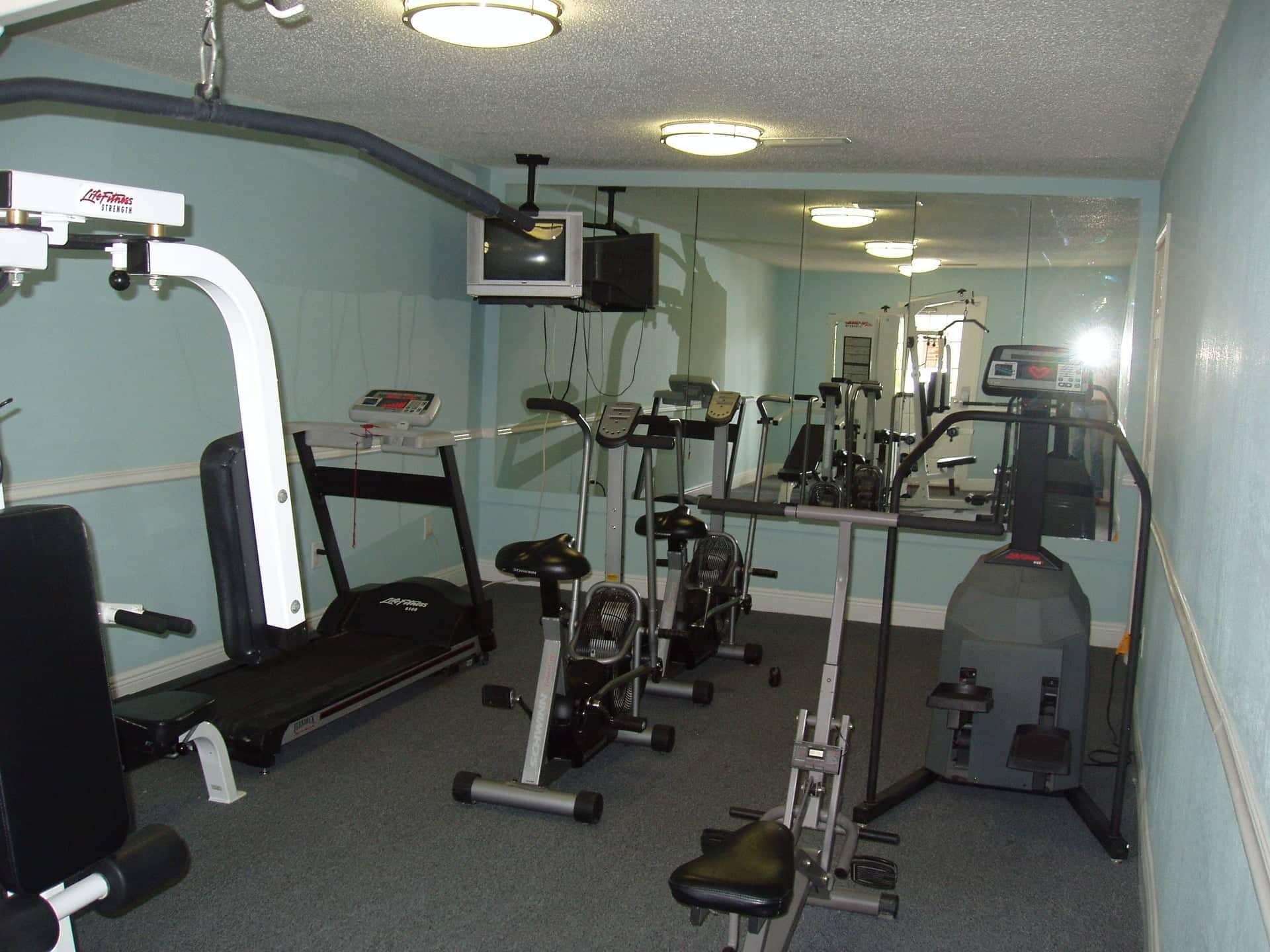 Een sportschool met cardioapparatuur, gewichten en een spiegelwand.