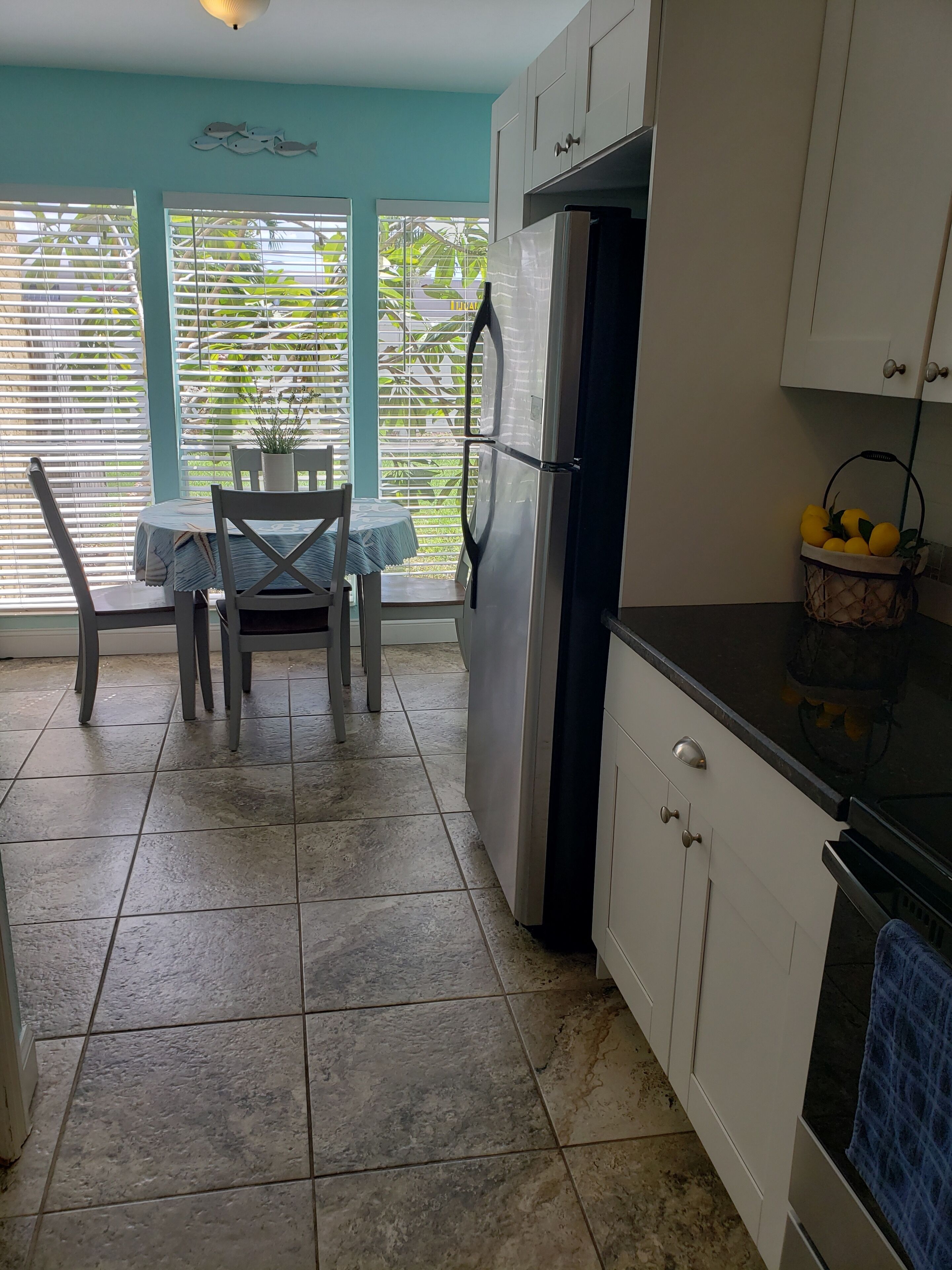 A kitchen with a dining table and chairs, a refrigerator, and a basket of lemons.