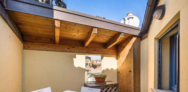 Ein Holzbalkon mit einem Blumentopf, einem Fenster und einem weißen Gebäude im Hintergrund.