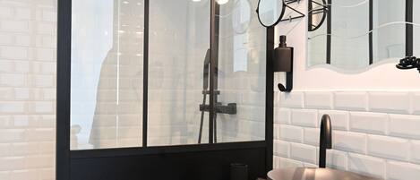 A modern bathroom with a black vanity, a round sink, and a glass shower enclosure.