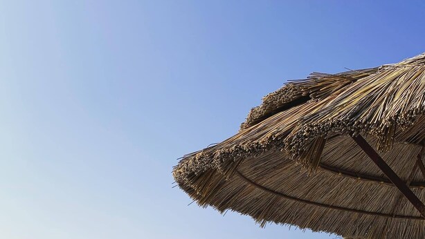 A beach with people sunbathing and swimming, a thatched umbrella, and a rocky breakwater.